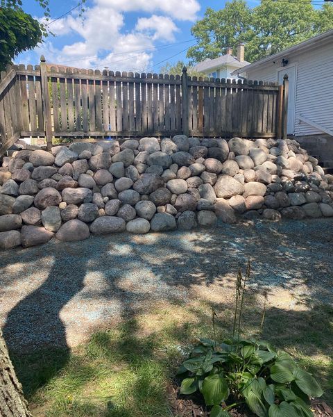 There is a large rock wall in the backyard of a house.