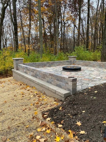 A stone patio with a fire pit in the middle of a forest.