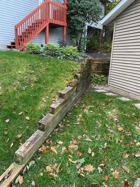 A wooden retaining wall in a yard next to a house with stairs.