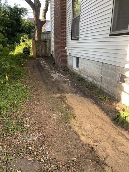 A dirt path leading to a house with a tree in the background.