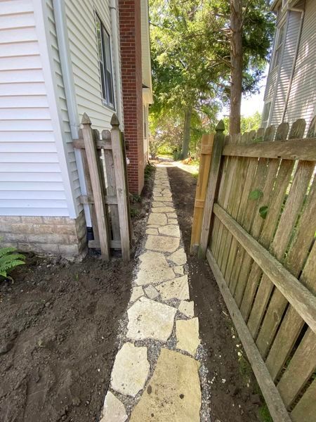 A stone walkway leading to a house next to a wooden fence.