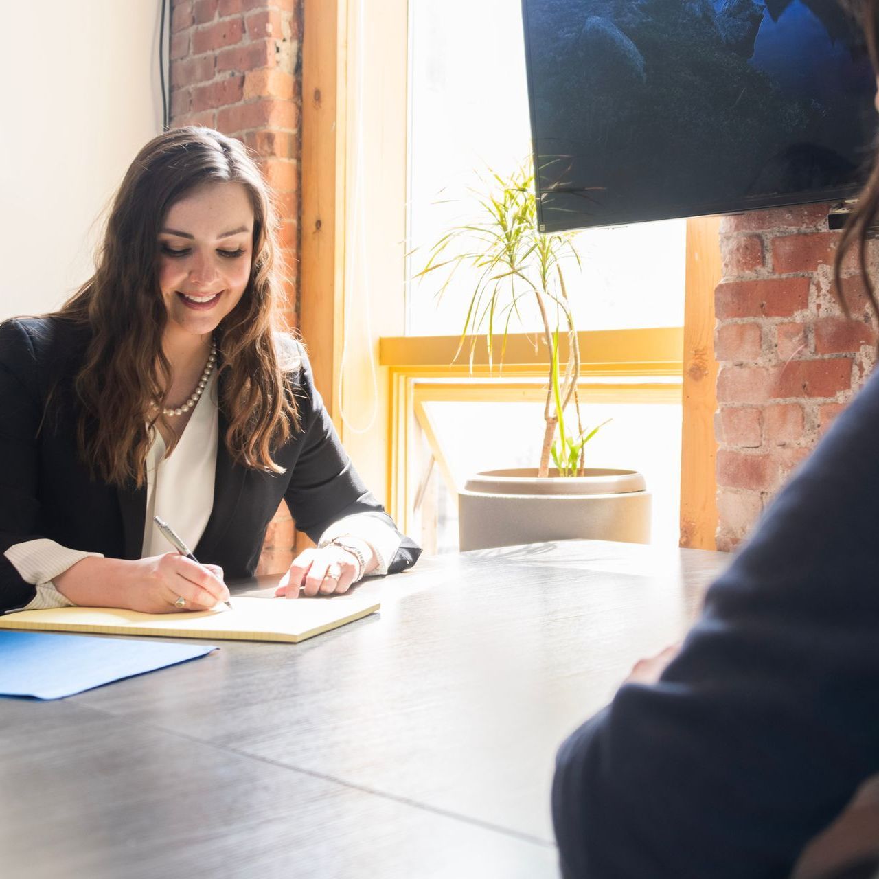 A woman is sitting at a table writing on a piece of paper