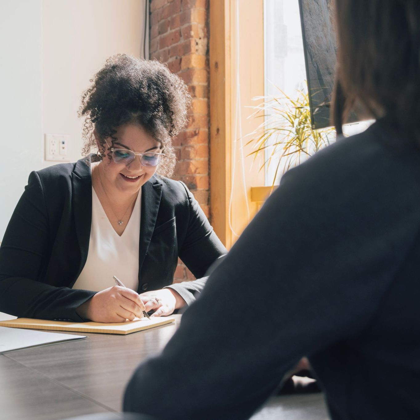 A woman is sitting at a table writing on a piece of paper.