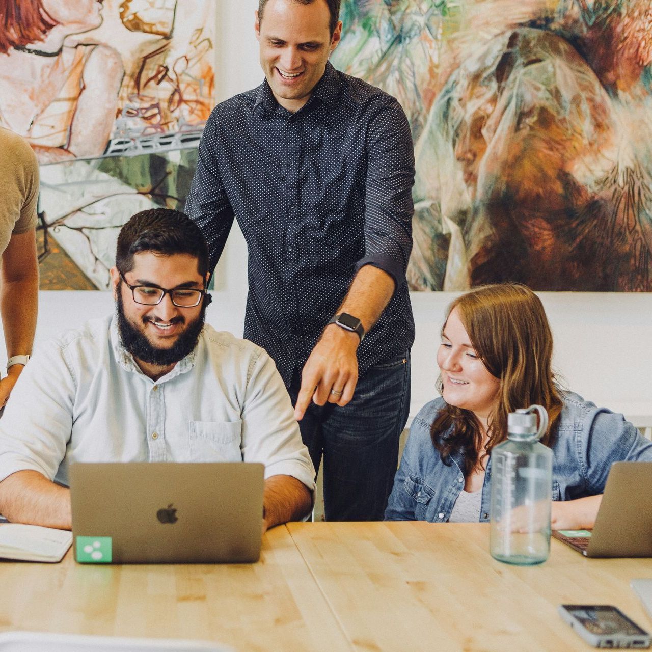A group of people are sitting around a table looking at a laptop