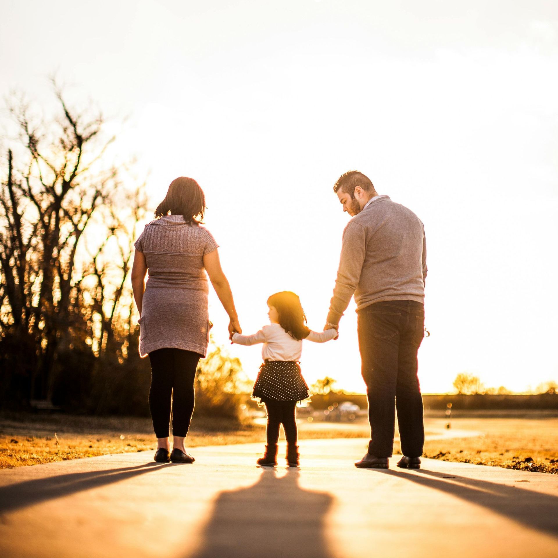 A family is walking down a sidewalk holding hands at sunset.