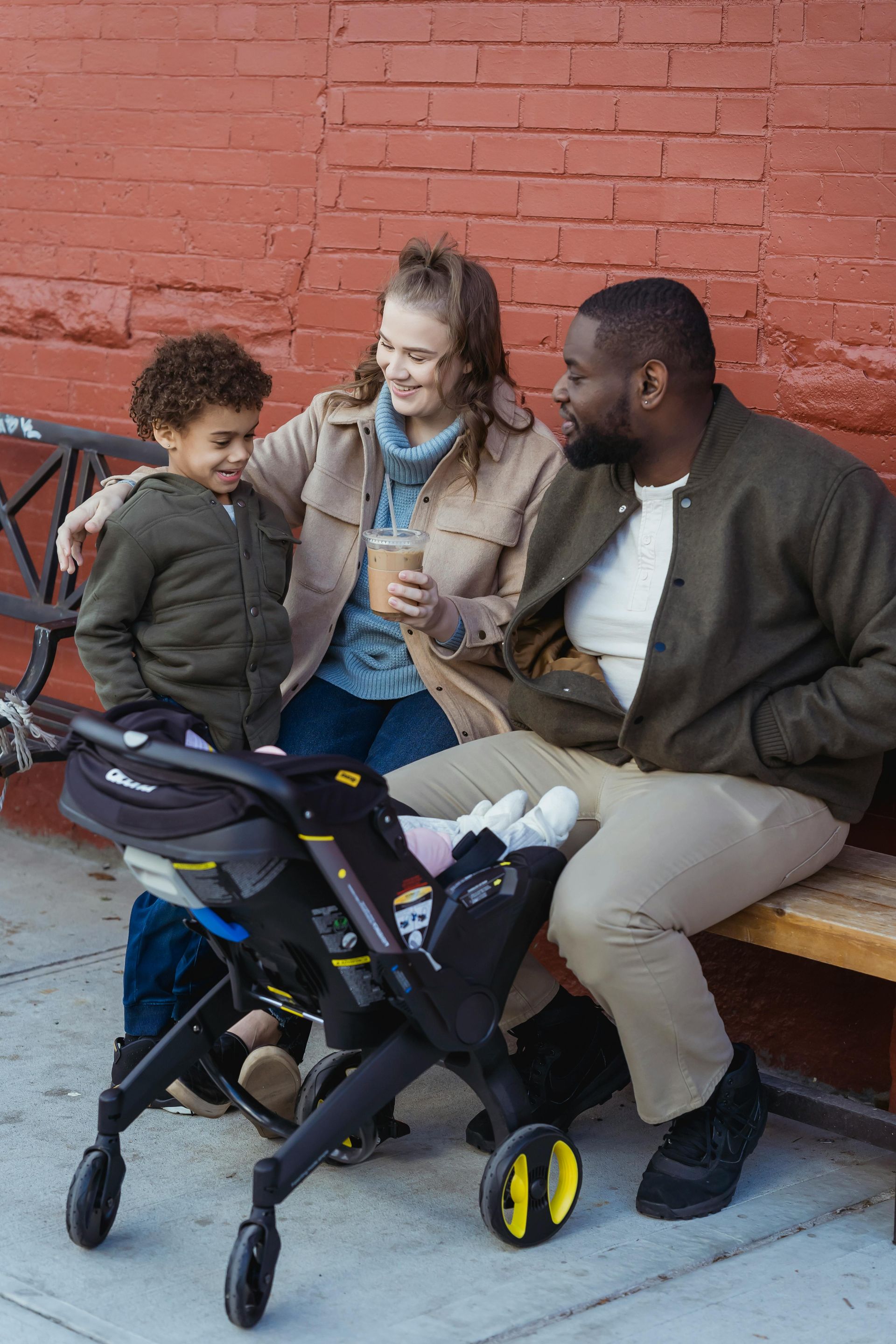 A man , woman and child are sitting on a bench with a stroller.