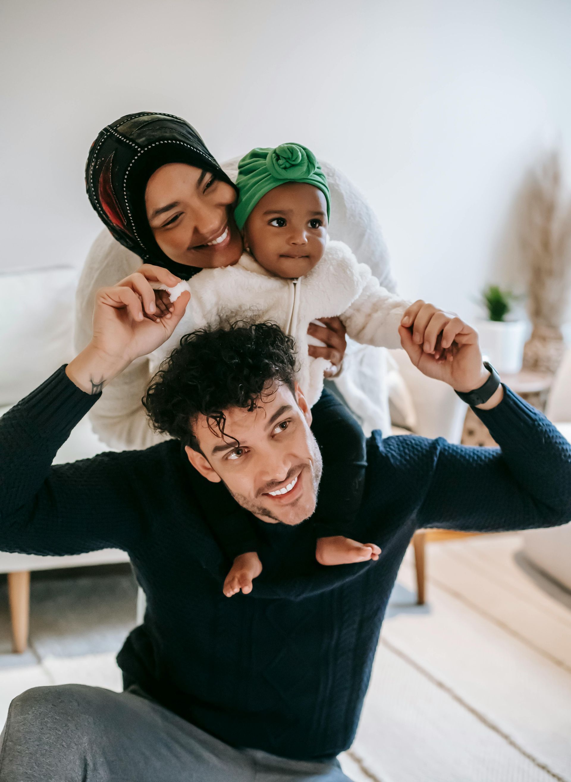 A man is carrying a baby on his shoulders in a living room.