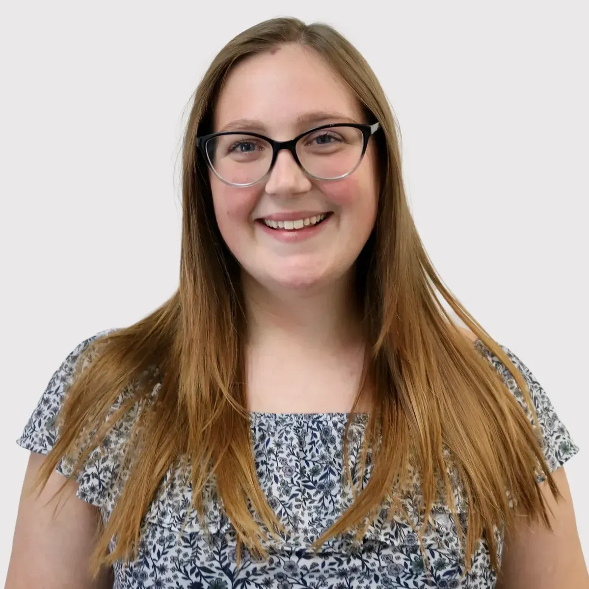 A woman wearing glasses and a floral shirt is smiling for the camera.