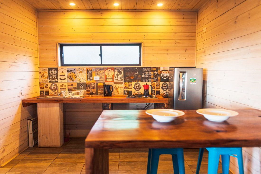 Cocina revestida de madera con mesa de madera, taburetes, fregadero, salpicadero estampado y una pequeña ventana.