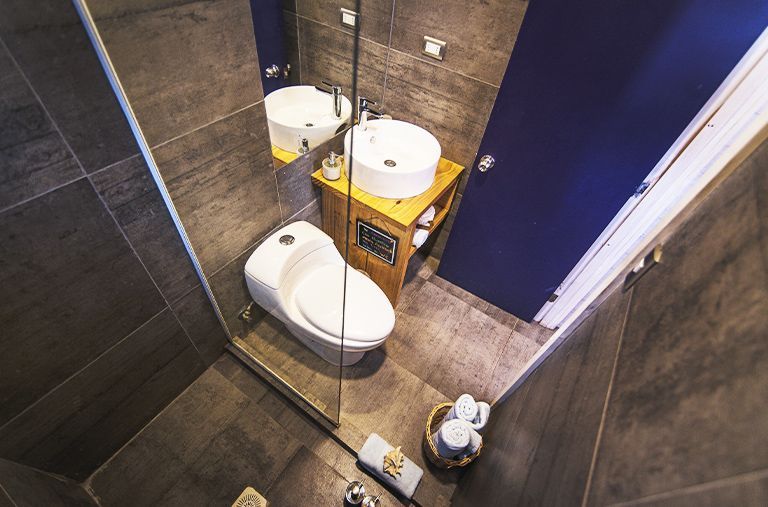 Baño pequeño con inodoro, lavabo, carrito de almacenamiento amarillo y puerta azul sobre suelo de baldosas.