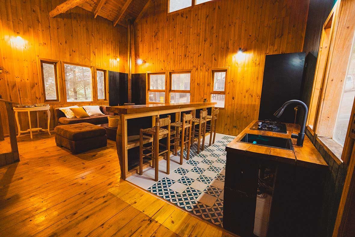 Cocina acogedora tipo cabaña con paneles de madera, isla central, taburetes de bar e iluminación cálida.