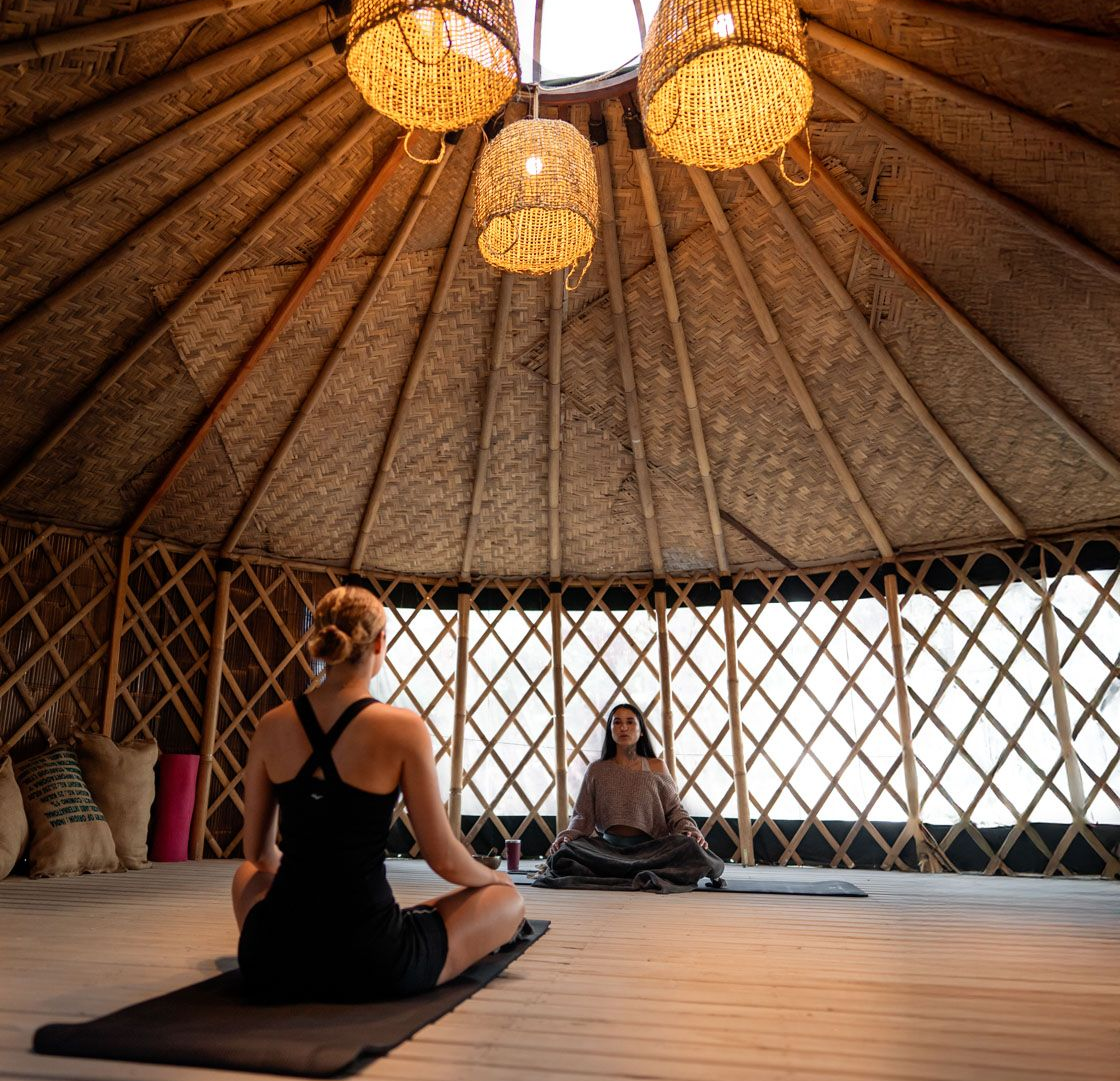 Personas meditando dentro de una yurta tejida bajo faroles colgantes.