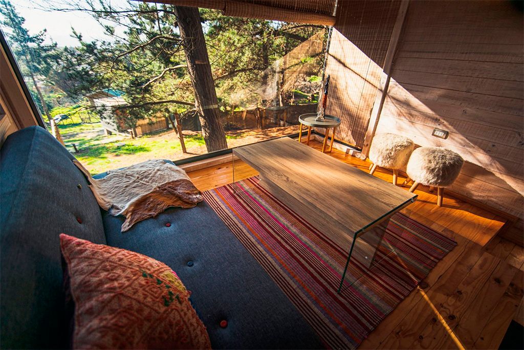 Acogedor porche con sofá azul oscuro, mesa de madera, alfombra estampada y vistas al jardín bañado por el sol.