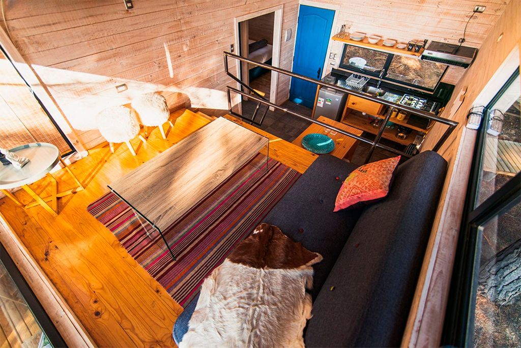 Sala de estar tipo loft con sofá, alfombra a rayas, mesa de madera y escritorio contra paredes de ladrillo visto.