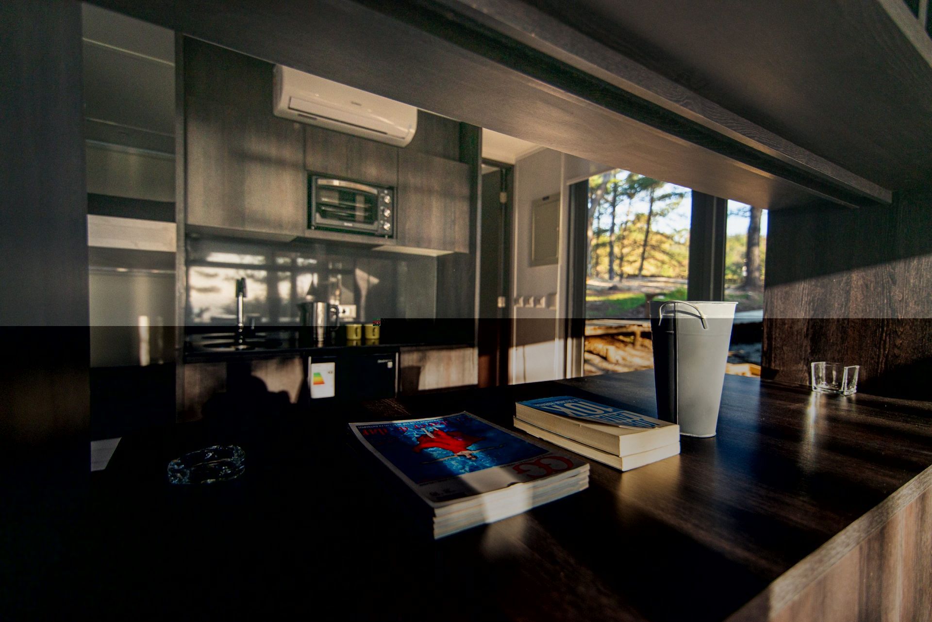 Salón moderno con una mesa baja, cojines azules y una luminosa ventana con vistas a los árboles del exterior.