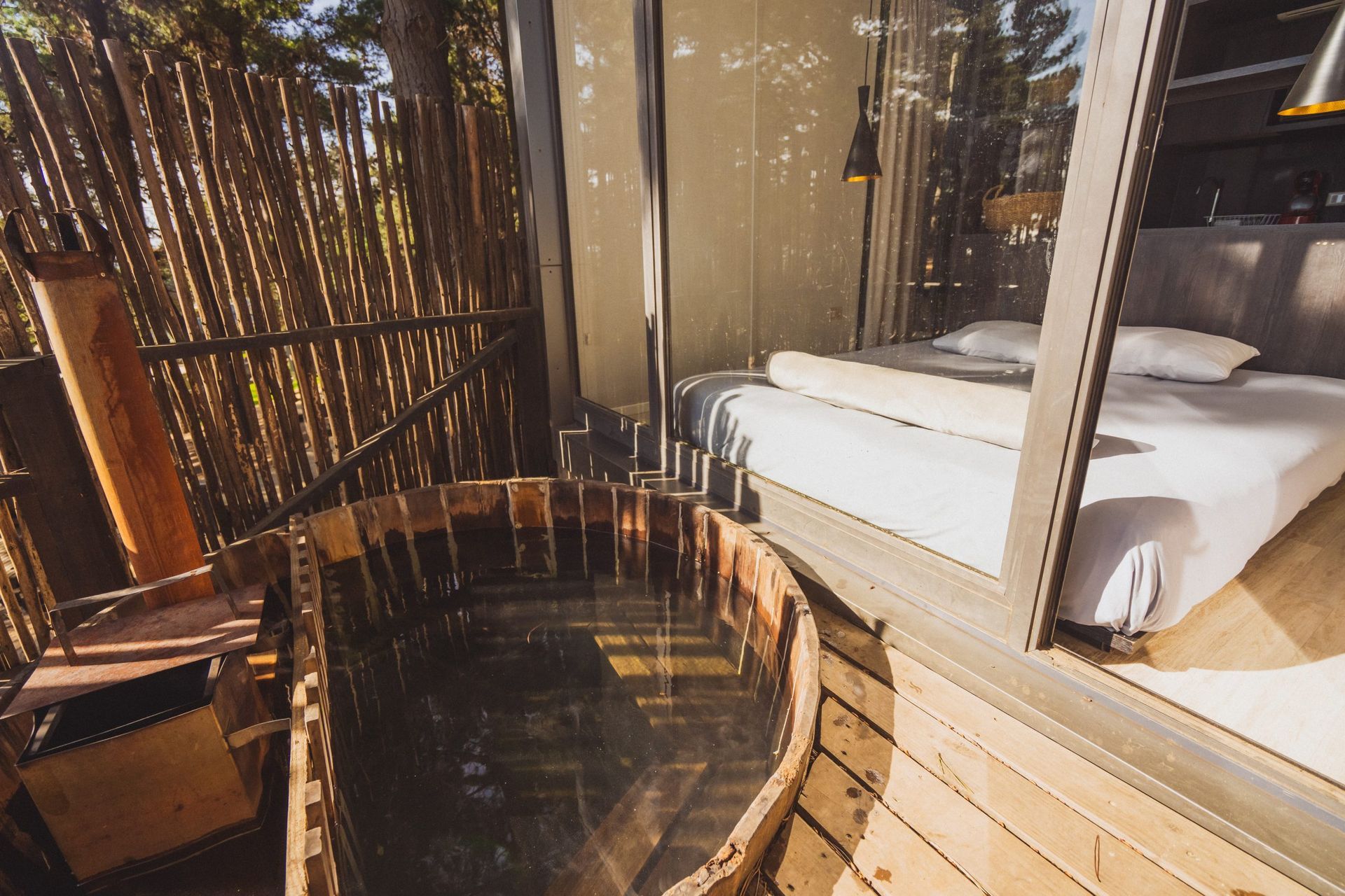 Bañera de hidromasaje de madera al aire libre junto a la cama en una cabaña rústica privada.