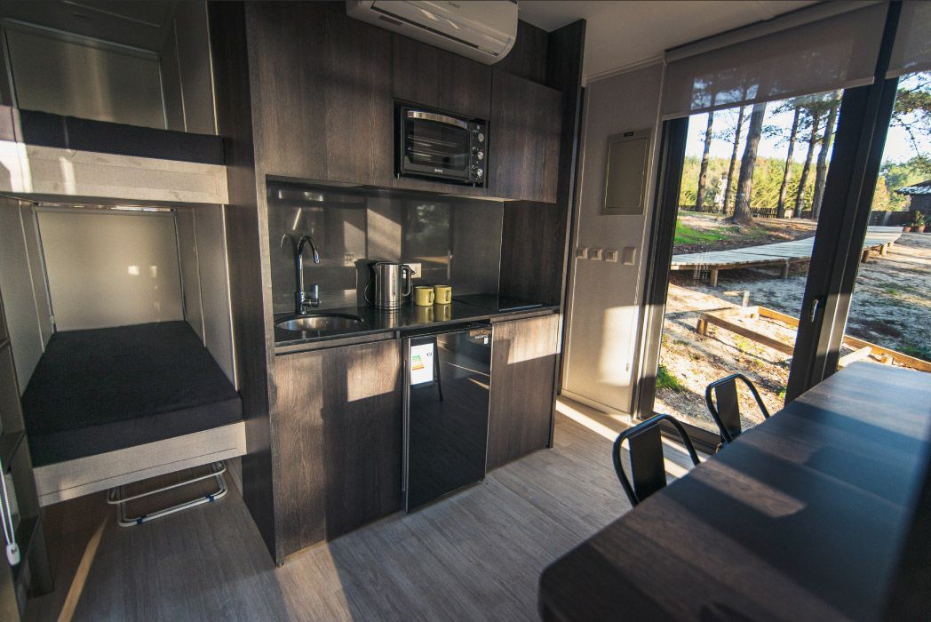 Una cocina moderna con gabinetes de madera oscura, un fregadero, con vista a un paisaje exterior iluminado por el sol.