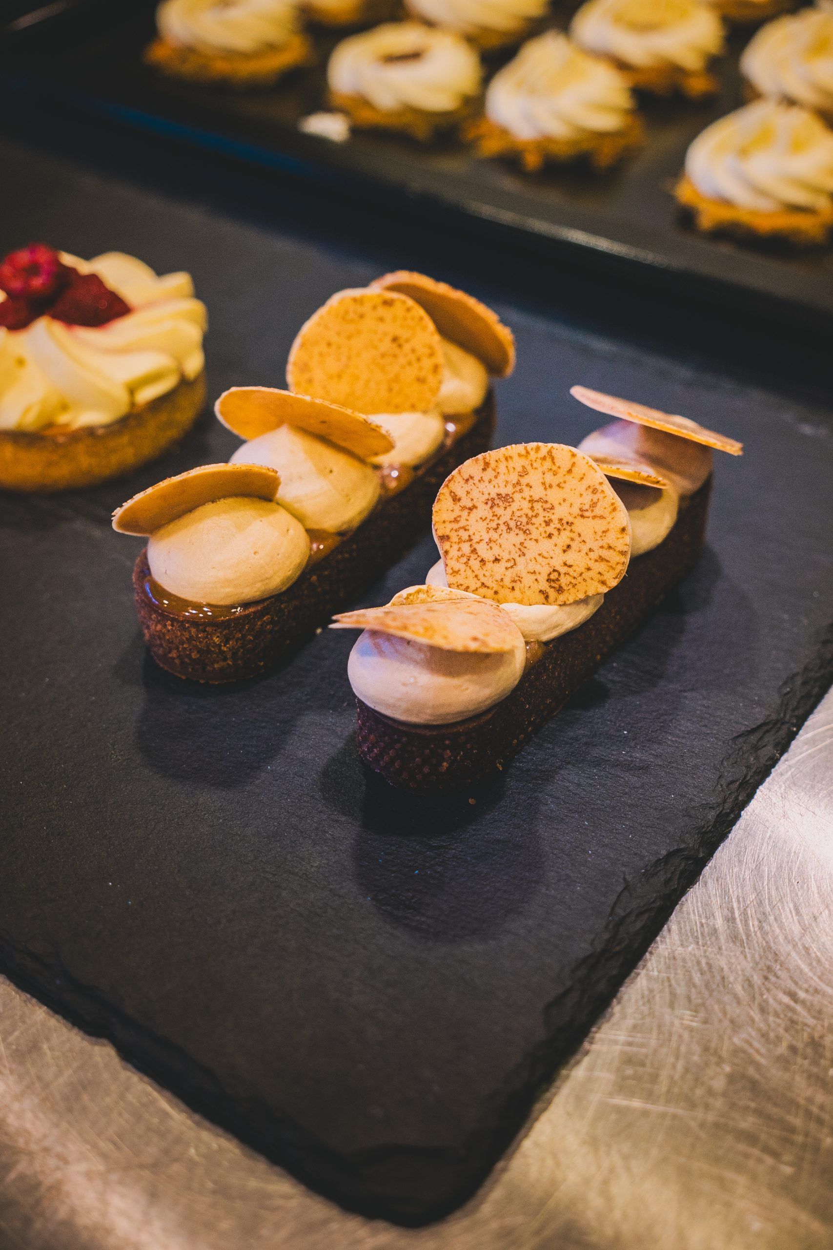 Pasteles artesanales con crema y finas patatas fritas dispuestos en una bandeja de piedra oscura para servir.