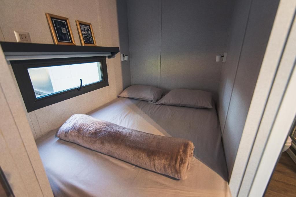 Un dormitorio pequeño y acogedor con una cama doble cuidadosamente hecha con sábanas grises y una almohada marrón mullida.