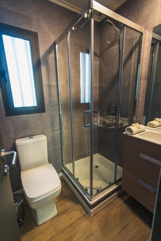 Un baño moderno con ducha de esquina de vidrio, inodoro blanco, tocador y piso de baldosas con apariencia de madera.