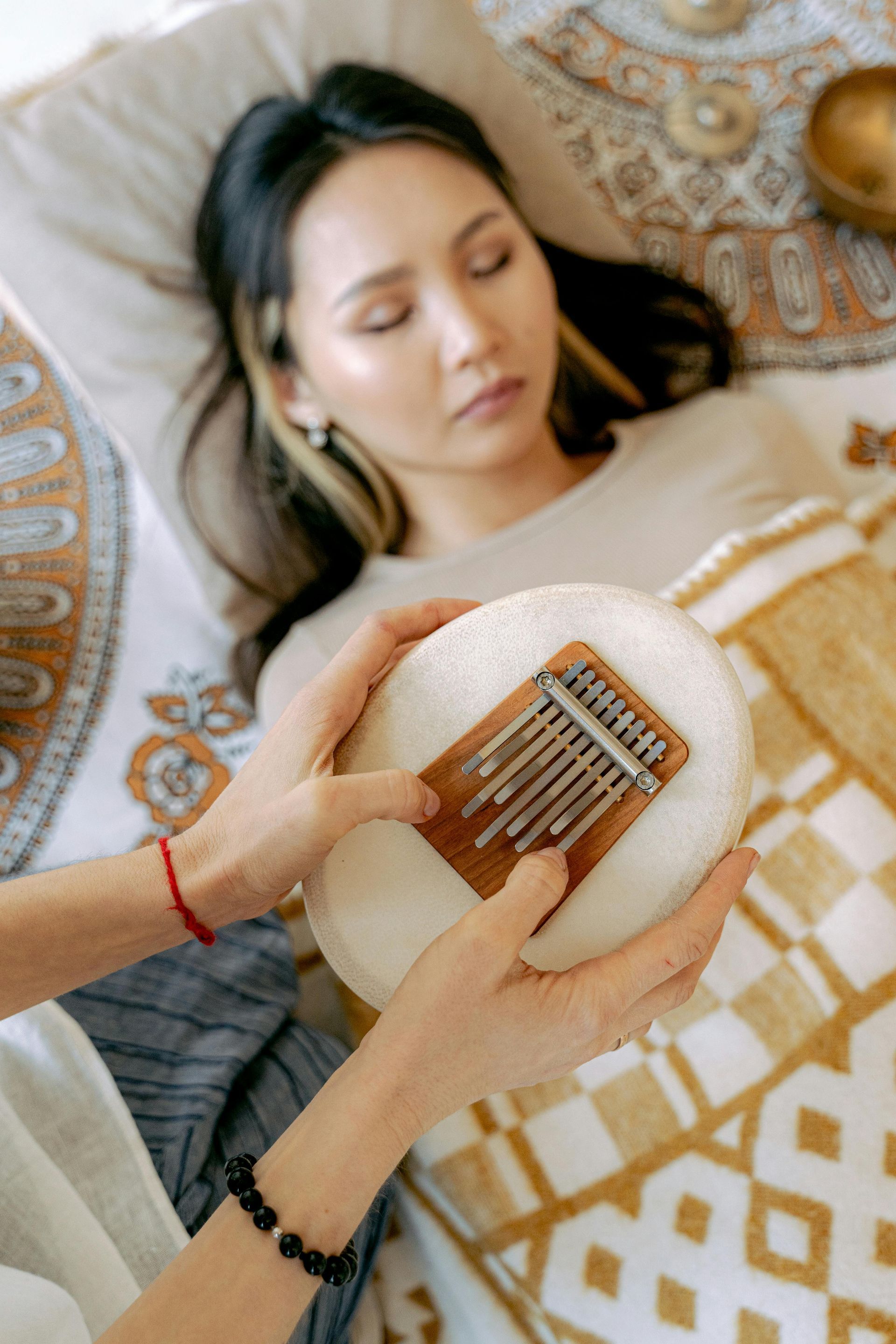 Unas manos tocan un pequeño instrumento sobre una persona dormida bajo una manta estampada.
