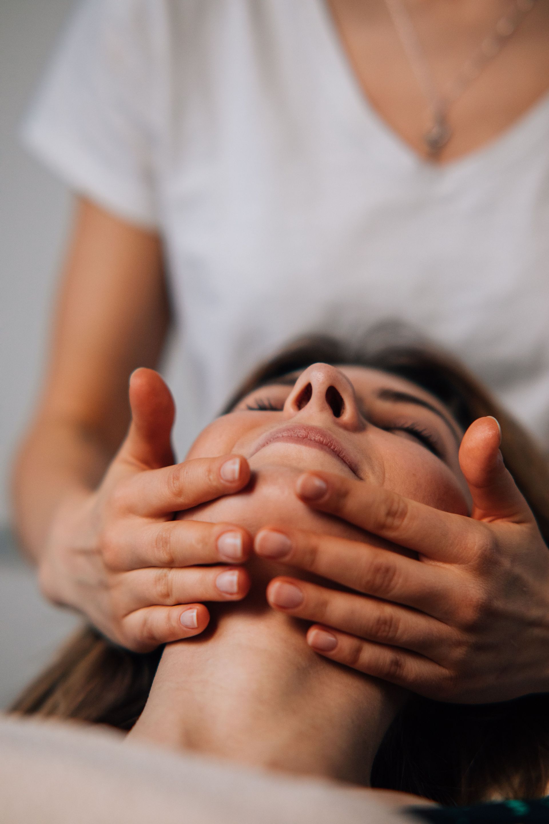 Persona que recibe un masaje facial con las manos cubriéndole el rostro, vistiendo una camisa blanca.