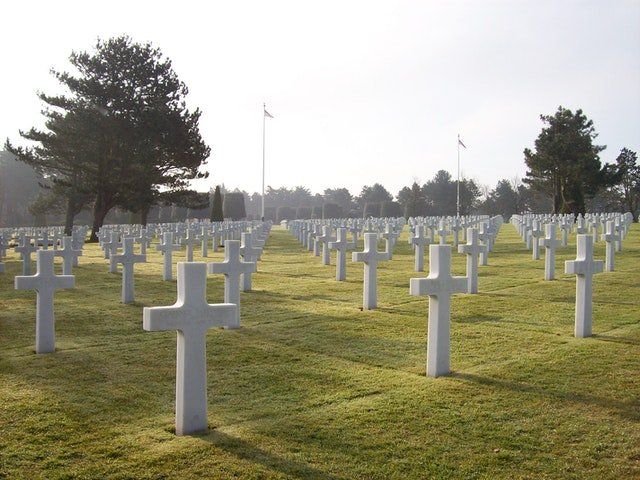 Rows of white crosses in a military cemetery on a grassy field at sunrise
