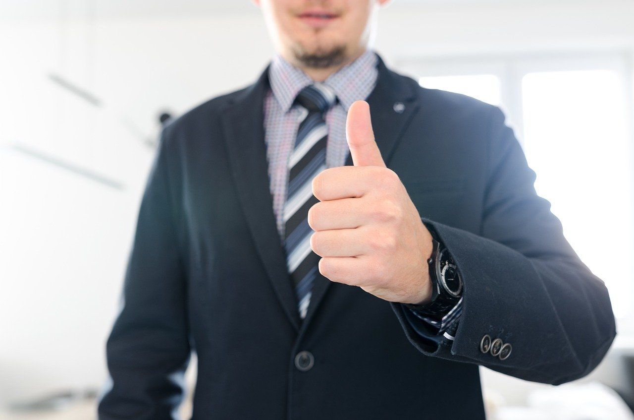 Businessperson in a suit giving a thumbs-up in a bright office setting