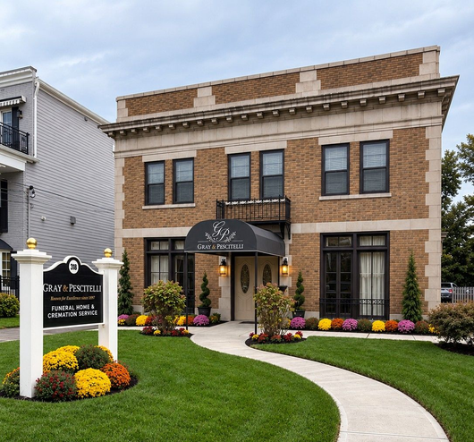 Brick office building with green awnings, trees, shrubs, and a paved parking lot under a blue sky