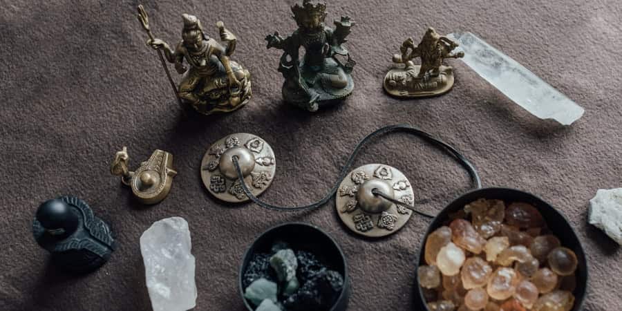 Small figurines and crystals arranged on a gray woven surface, with stones and a shell dish.