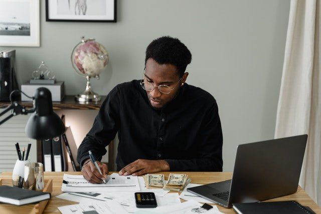 Person working at a desk with papers, cash, calculator, and laptop in a home office