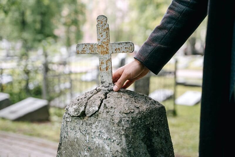 Hand placing a cross on a cracked gravestone in a cemetery