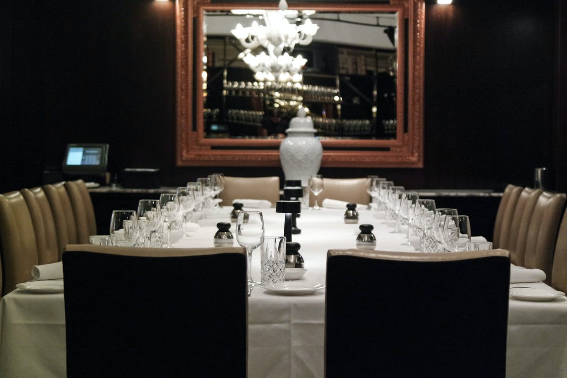 Elegant restaurant dining table set with white tablecloth, glassware, candles, and a large mirror chandelier reflection
