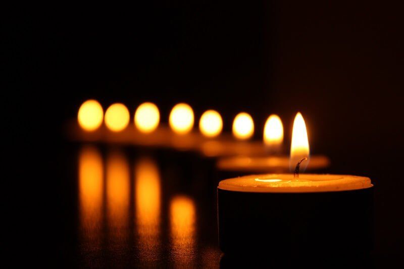 A row of glowing candles on a dark reflective surface, with one candle in the foreground.