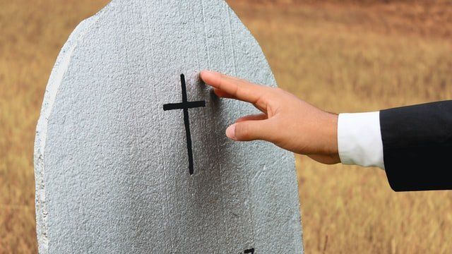 Hand placing a finger on a black cross marked on a gray gravestone