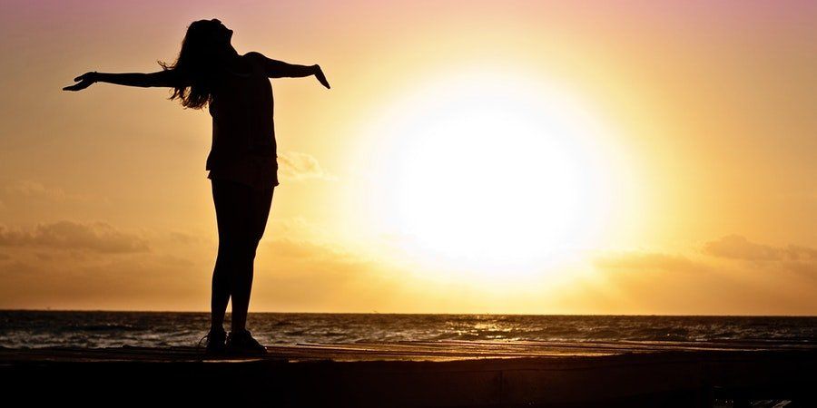 Silhouette of a person with arms outstretched at sunset by the ocean
