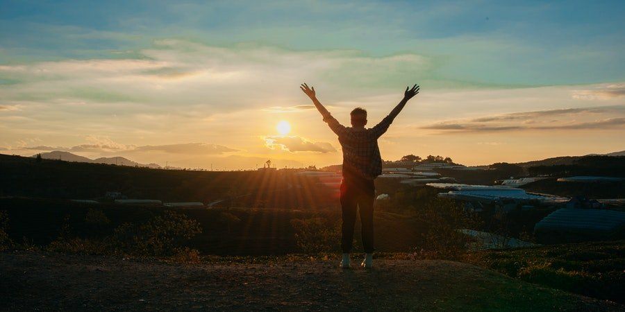 Silhouette of a person with raised arms at sunset over a coastal landscape