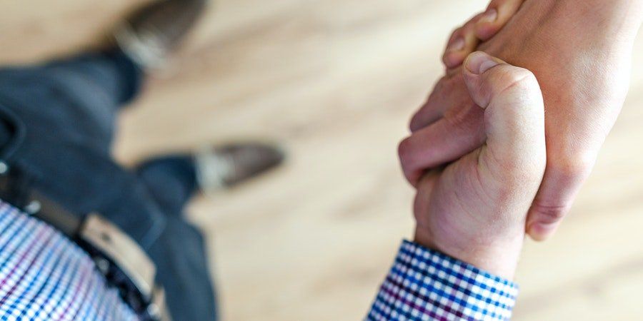 Two people clasping hands in a supportive handshake over a light wooden floor