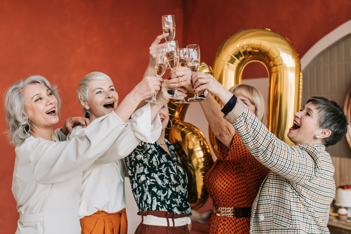 Four friends toasting with glasses in front of gold balloons at a party