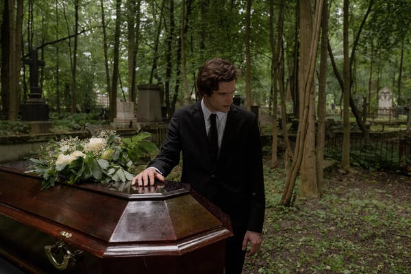 Mourners beside a coffin with white flowers in a forest cemetery