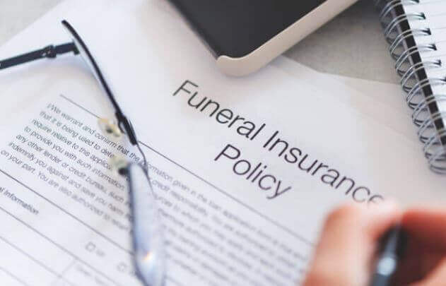 Funeral insurance policy document on a desk with eyeglasses and a hand writing beside it