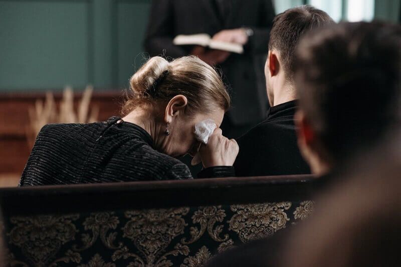 Person wiping tears while seated in a dim church pew during a solemn service