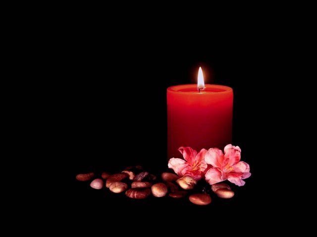 Red candle burning with pink flowers and scattered coffee beans on a black background