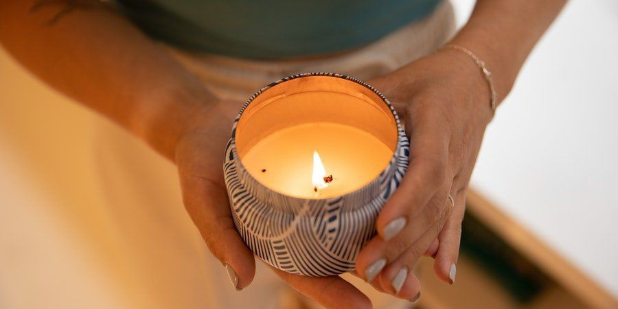 Hands holding a lit candle in a patterned holder