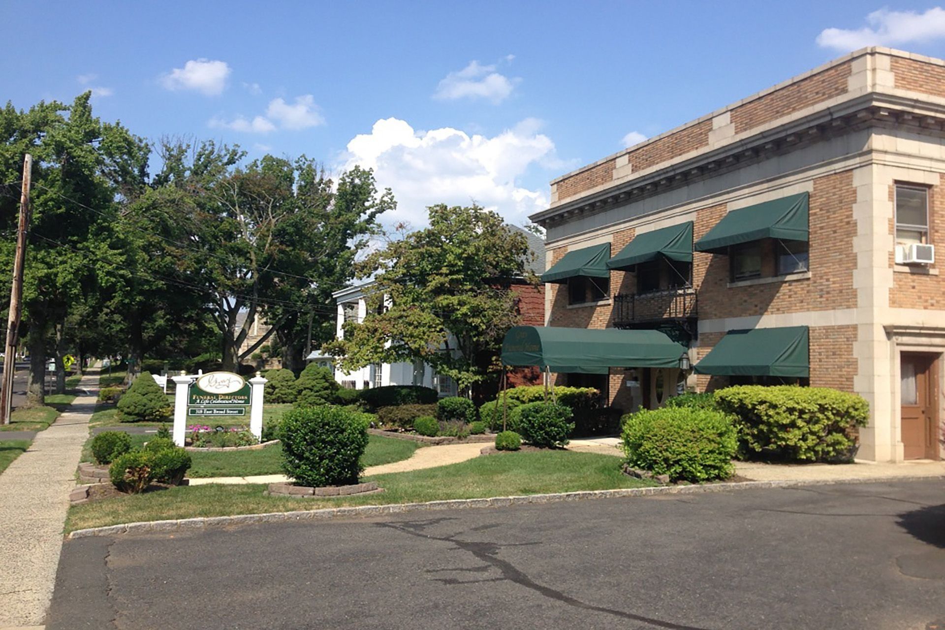 Brick office building with green awnings and landscaping beside a parking lot