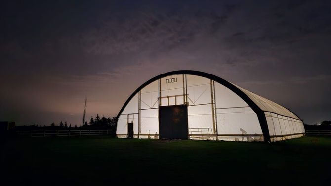 Glowing white Quonset hut at dusk in an open field beneath a dark sky