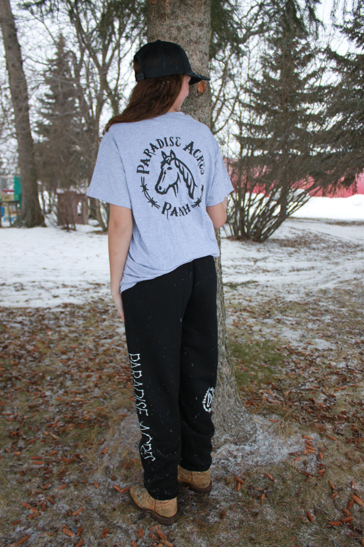 Person walking away on a snowy path, wearing a black cap, gray T-shirt, and black pants.