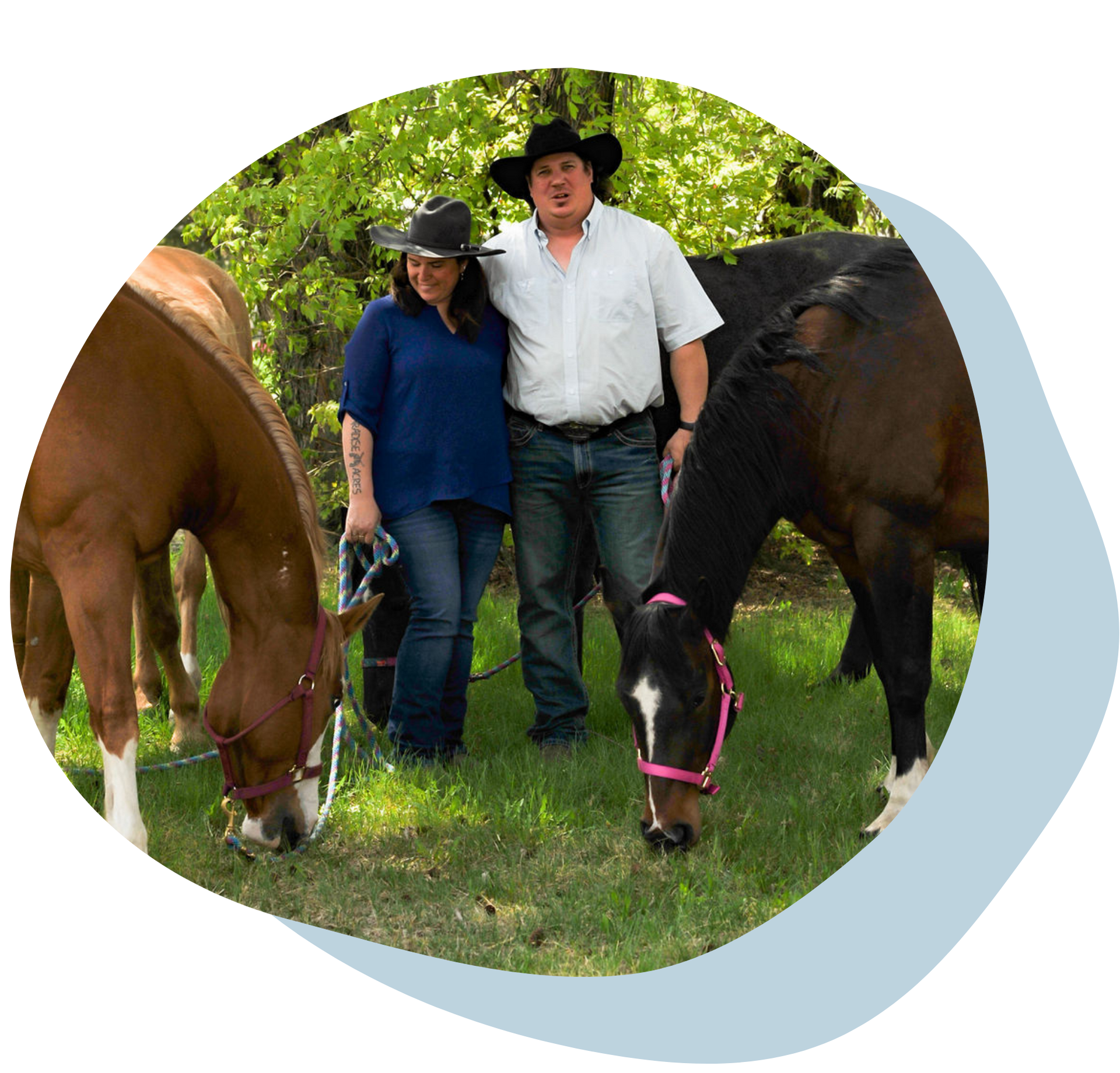 Two people standing with grazing horses outdoors under green trees