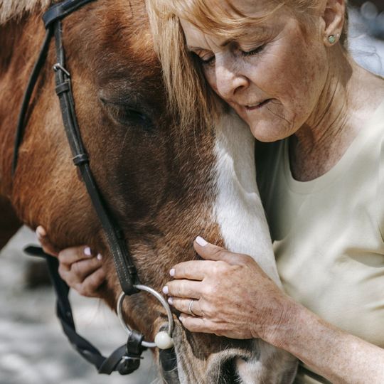 Woman gently holding a brown horse’s face with a white blaze, close-up outdoors
