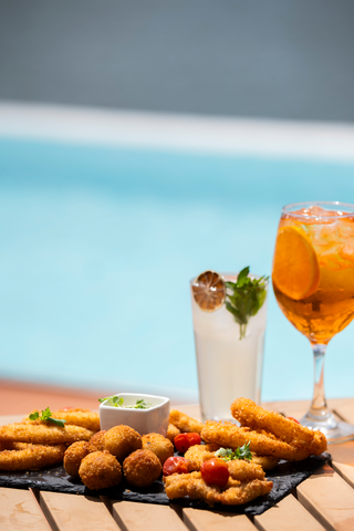 Un plato de comida y bebida en una mesa junto a una piscina.